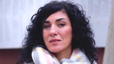 Kıvırcık siyah saçlı, atkı ve palto giyen, açık havada gülümseyen bir kadın. Modern yaşam tarzı, şık moda ve kentsel çevrede doğal ışık ile pozitif enerji.