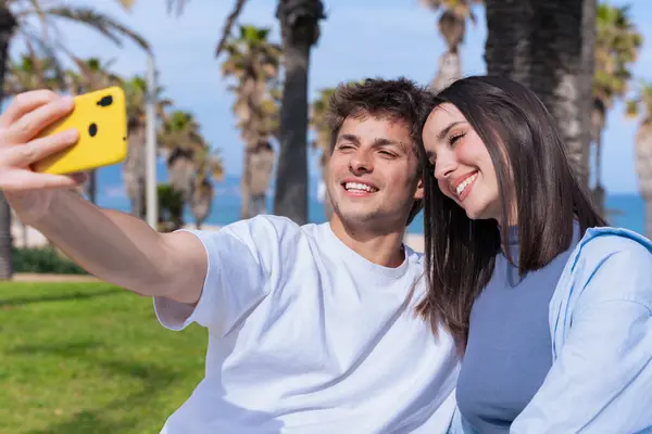 Mutlu genç çift, güneşli bir sahil gezintisinde eğlenceli bir selfie için poz veriyor, o parlak sarı bir akıllı telefon tutarken, o da yaz havasını yakalıyor, seyahat anılarını, aşkı yakalıyor.. 