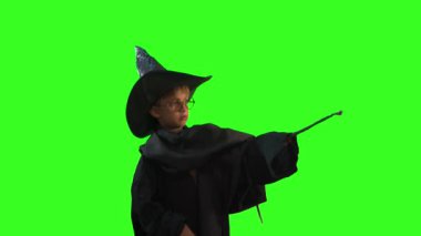 Yeşil arka planda sihirli değneği olan cadılar bayramı kostümlü bir çocuk.