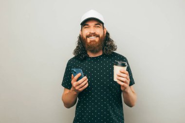 Sakallı bir adamın beyaz şapkalı ve elinde bir fincan kahve tutarken çekilmiş fotoğrafı..