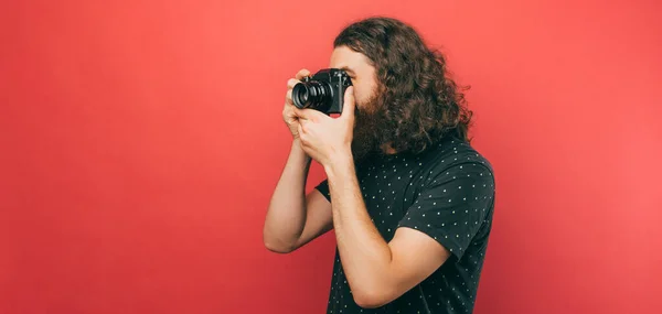 Side view photo of bearded hispter man with long hair making a photo with camera over pink background.