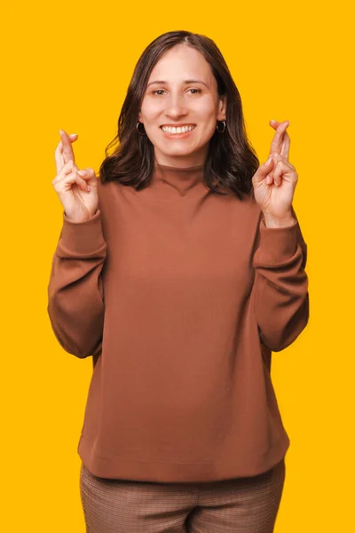 笑着的年轻美丽女子在黄色背景上交叉手指以求好运的垂直图像 — 图库照片