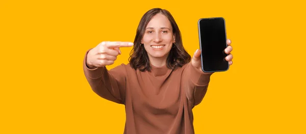Imagem Jovem Mulher Sorridente Apontando Para Smartphone Sobre Fundo Amarelo — Fotografia de Stock