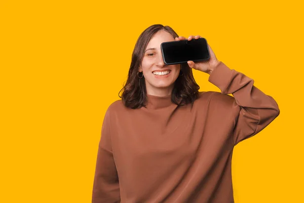 Portrait Young Woman Holding Smartphone Eyes Smiling Yellow Background — Stock Photo, Image