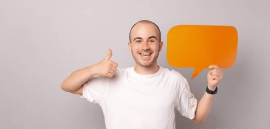 Beyaz tişörtlü hayret verici genç adam başparmağını kaldırıyor ve boş konuşma balonu tutuyor..