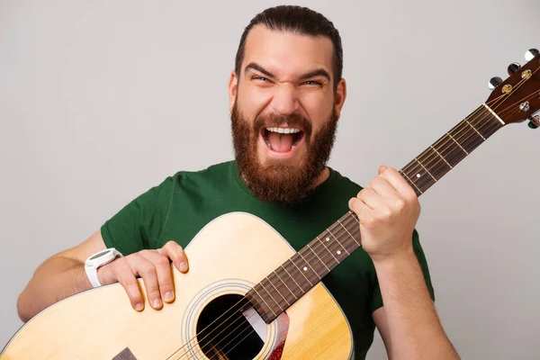 Zdjęcie Zdumionego Brodatego Mężczyzny Zielonej Koszulce Trzymającego Gitarę Akustyczną — Zdjęcie stockowe