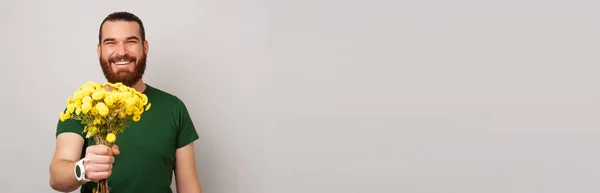 Фотографія Молодого Красивого Бородатого Чоловіка Зеленій Футболці Дарує Жовті Квіти — стокове фото