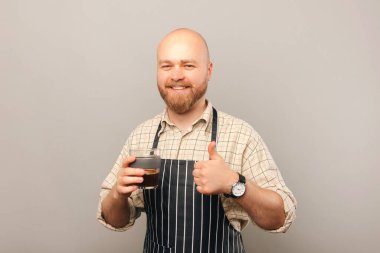 Kel bir barista, gri bir stüdyoda elinde bir bardak kahve tutarken kahvecisini tavsiye eder..