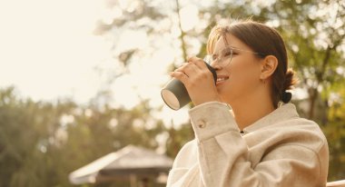 Açık havada sabah kahvesini yudumlayan mutlu genç bir kadının fotoğrafını çek. .