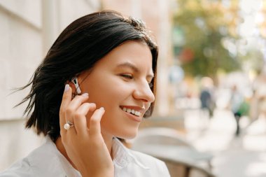 Şehir arka planında kulaklık takan sıradan bir genç kadının portresini kapat..