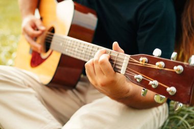 Bir adamın yeşil çimenlerde otururken karısı için akustik gitar çalmasını yakından çek..