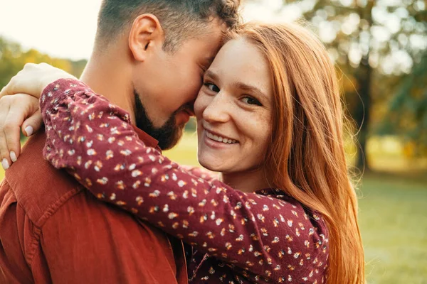 緑の公園で男を屋外で受け入れながら 赤い髪の女性はカメラに笑みを浮かべています — ストック写真