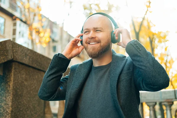 Ecstatic bald bearded man enjoys his headphones while going for a walk or sitting outdoors.