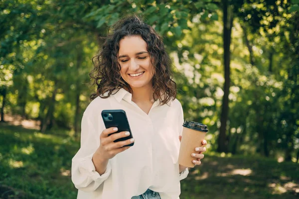 Sorrindo Alegre Jovem Caucasiana Usando Smartphone Livre Parque Segurando Xícara — Fotografia de Stock