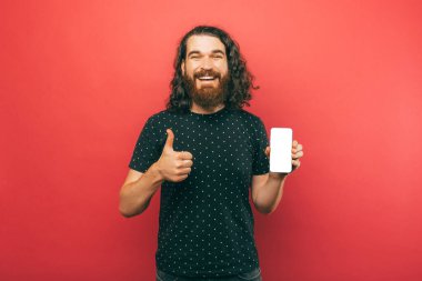 Yakışıklı sakallı adam elinde tuttuğu telefon ekranında gösterilen yeni mobil uygulamayı onaylıyor.