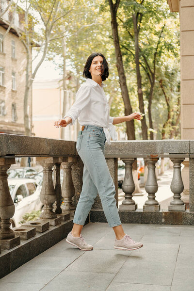 Полный снимок очаровательной молодой женщины, идущей на балкон в прекрасный день.