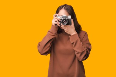 Sarı arka planda eski model bir kamerayla fotoğraf çeken genç bir kadının yakın plan fotoğrafı..