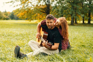 Genç çift yeşil çimenlerde otururken bir parkta gitar çalarak vakit geçiriyorlar..