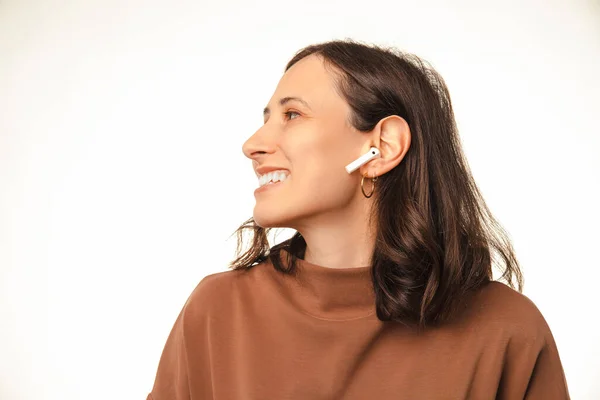 Close up shot of a wide smiling woman is wearing wireless headphones ear pods. Studio shot over white background.