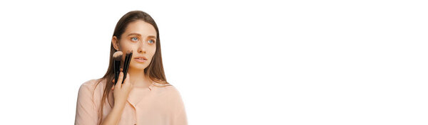 Баннерный портрет молодой блондинки, держащей кисти возле лица на белом фоне.