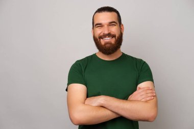 Yeşil giyen mutlu, kendine güvenen adam güçlü kollarını kavuşturup kameraya gülümsüyor..