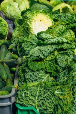 Markette çekilmiş taze yeşil lahana yaprakları ve salatalıkların dikey fotoğrafı..