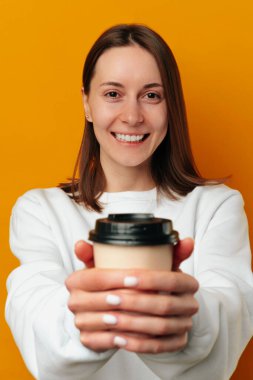Vertical crop shot of a young woman holding tight a to go cup of coffee over yellow background.