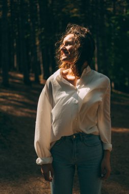 Vertical shot of a young curly woman enjoying windy sunny weather in a forest.
