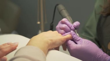 Close up footage of specialist removing gel nail polish from manicure with electrical drill machine.