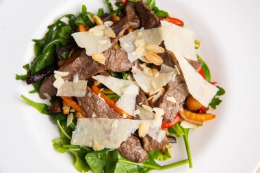Top view of a warm salad with rucola beef steak slices parmesan and slices of nuts.