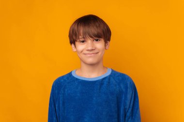 Studio portrait of a cute young teenager boy wearing blue and smiling over yellow backdrop.