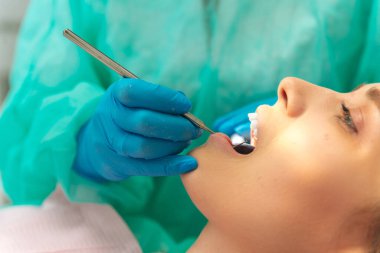 Close up side view shot of a blonde woman with open mouth at the dentist with blue gloves.