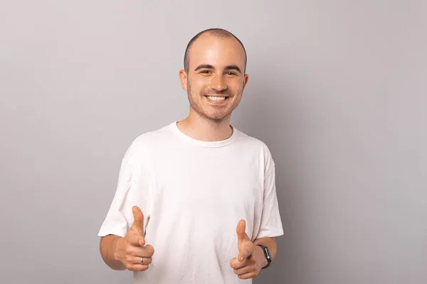 Young smiling balding man is pointing at you or at the camera with two index fingers.