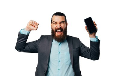 Young overjoyed bearded man wearing jacket shouts as a winner while holding his phone.