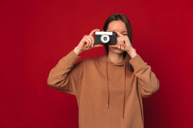 Güzel genç bir kadın hobisine çalışıyor ve fotoğraf makinesiyle fotoğraf çekiyor. Stüdyo çekimi kırmızı arkaplanda.