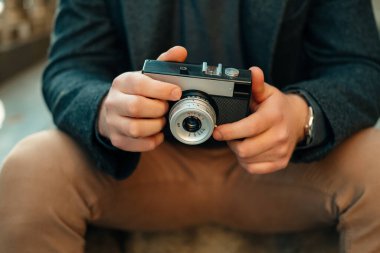 Bir erkeğin dışarıda otururken elinde antika bir kamera tutarken yüzsüz görüntüsü..