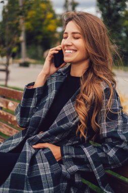 Neşeli kadın telefonda konuşuyor ve dışarıda bankta otururken gülüyor..