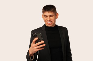 Studio shot of a young smiling man is looking at the phone he is holding over white background.