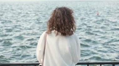 Footage of young curly woman standing in front of water waves and relaxing.