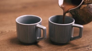 Close up video of barista pouring Turkish Coffee in two small cups on wooden background.