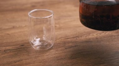 Close up video of barista pouring hot herbal tea in transparent glass over wooden background.