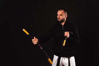 Portrait of a serious strong man performs some exercises with his nunchaku over black background.