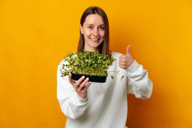I recommend these micro greens says a young smiling woman with thumb up over yellow background.