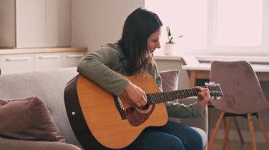 Footage of young woman practicing at acoustic guitar at home.