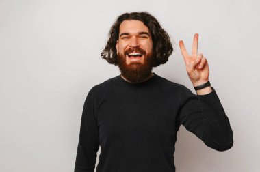 I am for peace says a young bearded man with long hair showing the v gesture. Studio portrait over gray background.