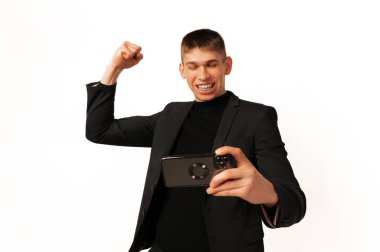 Excited man wearing jacket makes the winner gesture while looking at the phone he is holding.