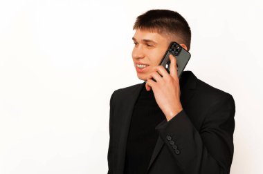 Young man wearing a black jacket is having a conversation over the phone over white background.