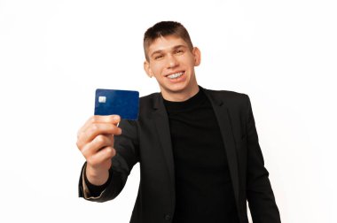 Cheerful young man wearing jacket is showing to the camera a blue credit card he is using.