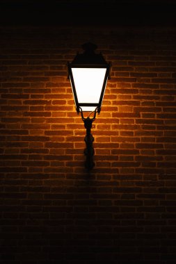 Gece vakti dışarıda sıcak bir lambayla tuğla duvarın dikey görüntüsü..
