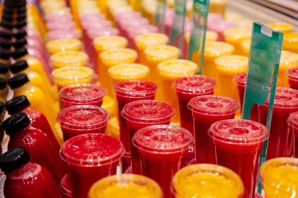 Colourful fresh natural fruit juices in plastic cup at the street market in Spain.